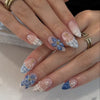 A close-up of a hand displaying pink flower almond press on nails with white and blue marbled designs.