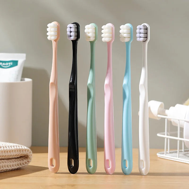 A set of five soft bristle toothbrushes in various pastel colors, including pink, black, mint green, and light blue, displaye