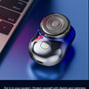 A small, round, metallic shaver in a blue casing rests on a dark surface next to a laptop keyboard.