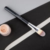 A black flat top kabuki foundation brush with a silver ferrule and light brown bristles resting on a black surface.