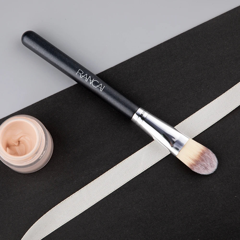 A black flat top kabuki foundation brush with a silver ferrule and light brown bristles resting on a black surface.