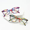A pair of retro cat eye reading glasses with multicolored, striped frames resting on a white block.