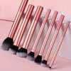 A set of seven professional makeup brushes with rose gold handles and black bristles arranged diagonally.