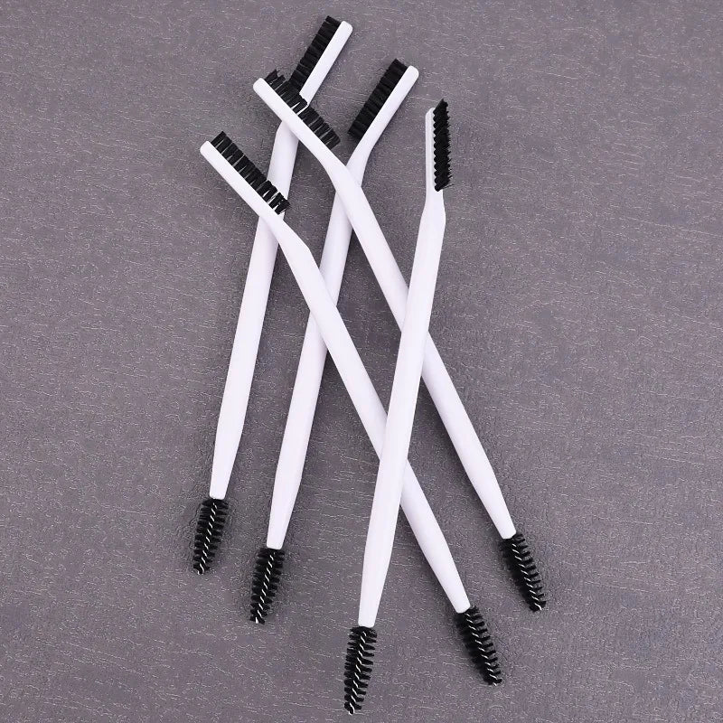 A set of white dual-ended eyelash curlers and brow brushes arranged diagonally on a gray surface.