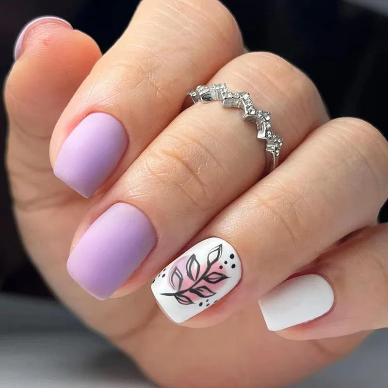 A hand displays a set of blue floral press-on false nails on a finger, with a silver ring visible.