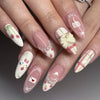 A close-up of a hand displaying pink heart pearl press-on fake nails with white and pink accents.