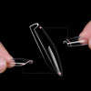 Une main tient un kit de pointes de ongles pressées noires, montrant diverses formes et tailles de pointes claires et opaques