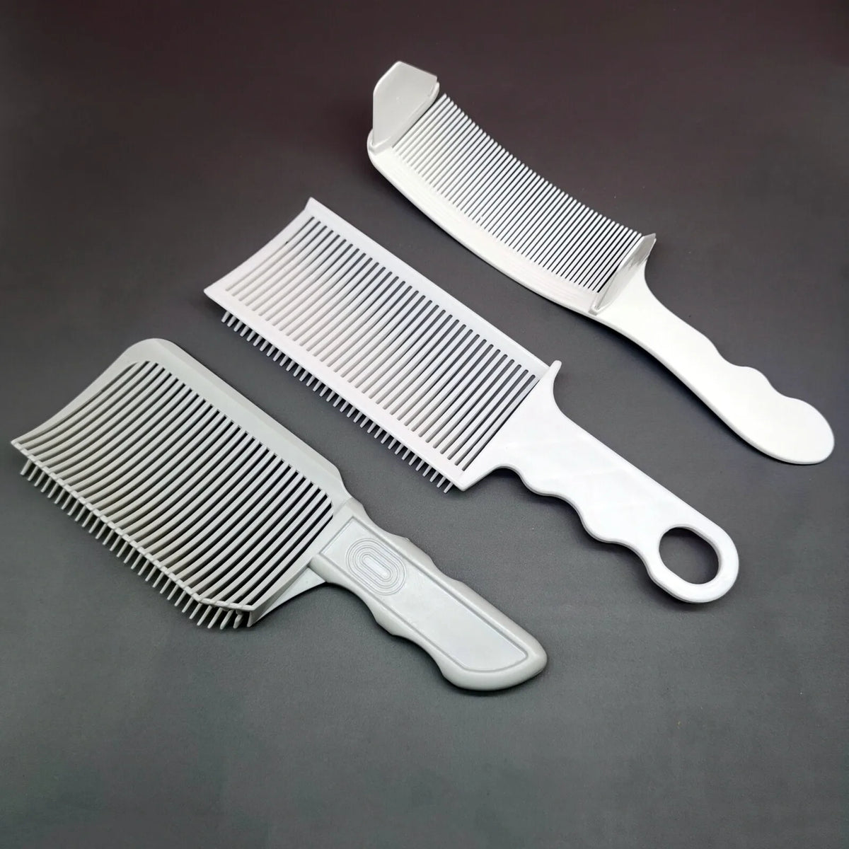 A set of three white professional flat top hair cutting combs displayed on a dark gray surface.