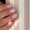 Close-up of a hand displaying pink and white striped press-on nails on an almond shape finger.