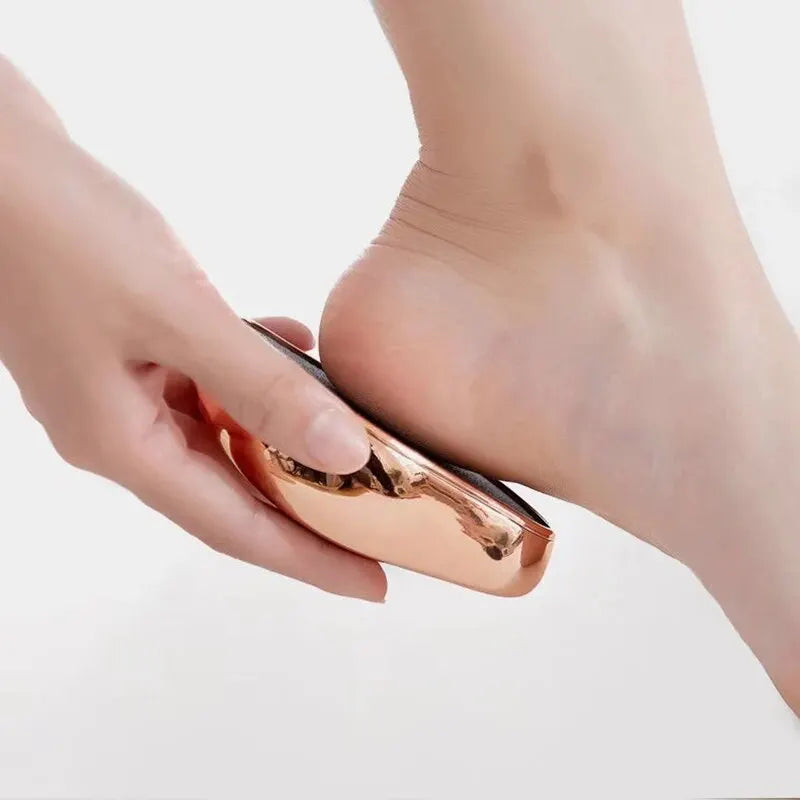 A hand holds a small, metallic glass foot file tool against the skin of a foot.