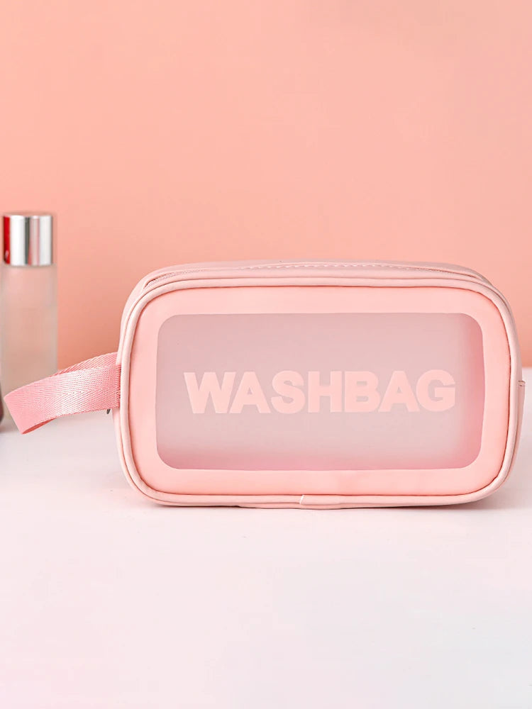 A pink cosmetic storage bag with a pink strap is displayed on a white surface next to a glass bottle.