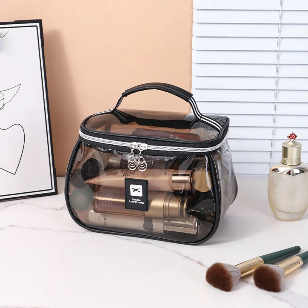 A clear cosmetic bag with a black zipper and handle containing various makeup brushes and tools.