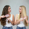 Two young women show off long hair using a pink detangling hair comb.
