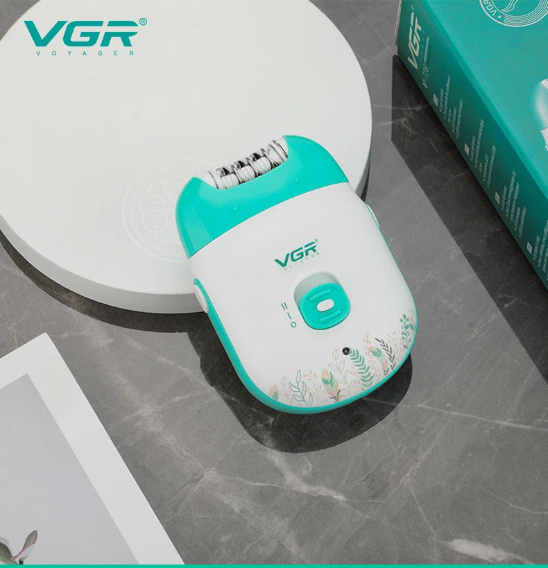 A white and teal VGR electric epilator device is shown on a gray surface next to its packaging box.