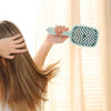 A hand is using a light blue professional detangling hair brush on long blonde hair near a window.