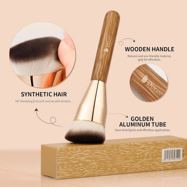 A golden aluminum tube foundation brush with a wooden handle and synthetic hair bristles shown next to its packaging box.