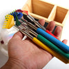 A hand holds a set of colorful stainless steel telescopic back scratchers inside a wooden box.