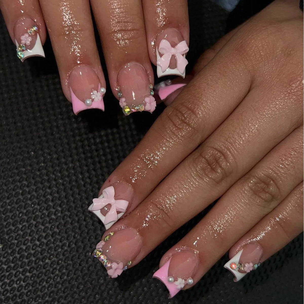 A hand displays nude pink press-on nails decorated with leopard print accents and 3D charms.
