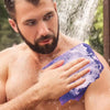 Un homme utilise une éponge exfoliante violette sur sa peau sous la douche.