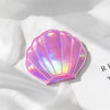 A pink iridescent seashell-shaped portable magnifying makeup mirror resting on a white surface.