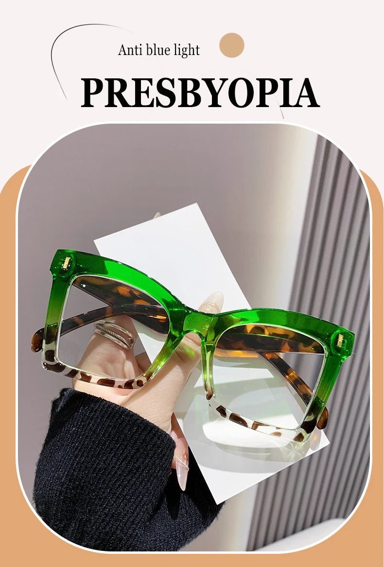 A pair of green-framed reading glasses with brown tortoiseshell lenses shown on a person's hand.