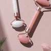 A set of rose gold and white jade gua sha tools with oval stones resting on a pink background.