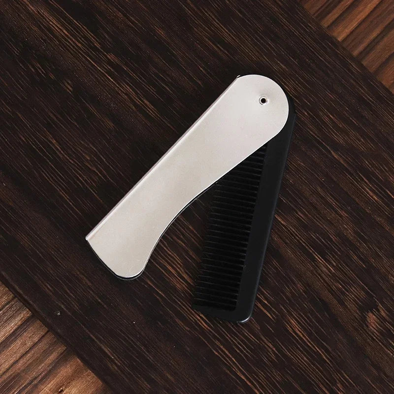 A silver foldable anti-static steel comb lying on a dark wooden surface.