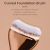 A close-up of a curved foundation brush with soft nylon bristles shown against a neutral background.