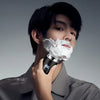 A man holds a white shaving foam on his face while using a black mini electric shaver.