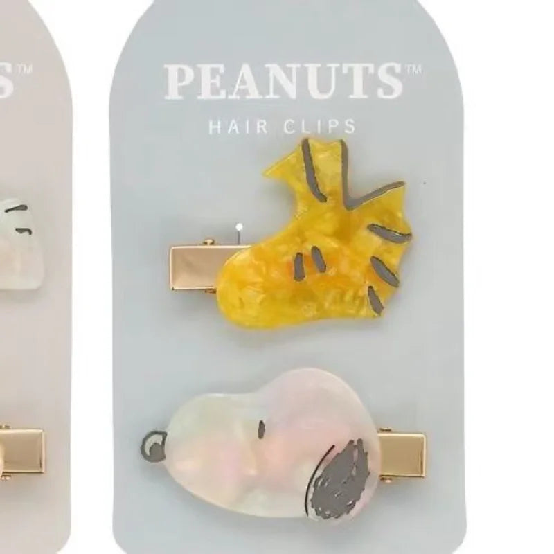 A set of Peanuts hair clips featuring a yellow hand and a pink face design.