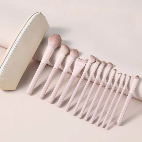 A set of professional loose powder makeup brushes with light pink handles and a cream-colored case.
