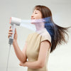 A woman is using a professional high-speed hair dryer to style her long, dark hair.
