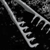 A white volumizing wide-tooth hair styling comb with teeth is shown against a dark background, surrounded by water droplets.