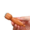 A hand holds a wooden gua sha tool with brass lotus eyes for facial massage.