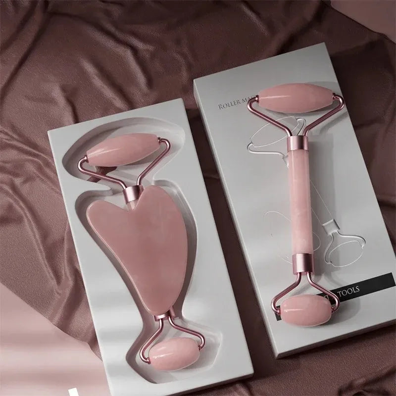 A set of pink jade gua sha facial tools displayed in white packaging on a brown fabric background.