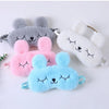 Un set de tres mascarillas de peluche con forma de conejo caricaturesco en gris, rosa y azul claro.