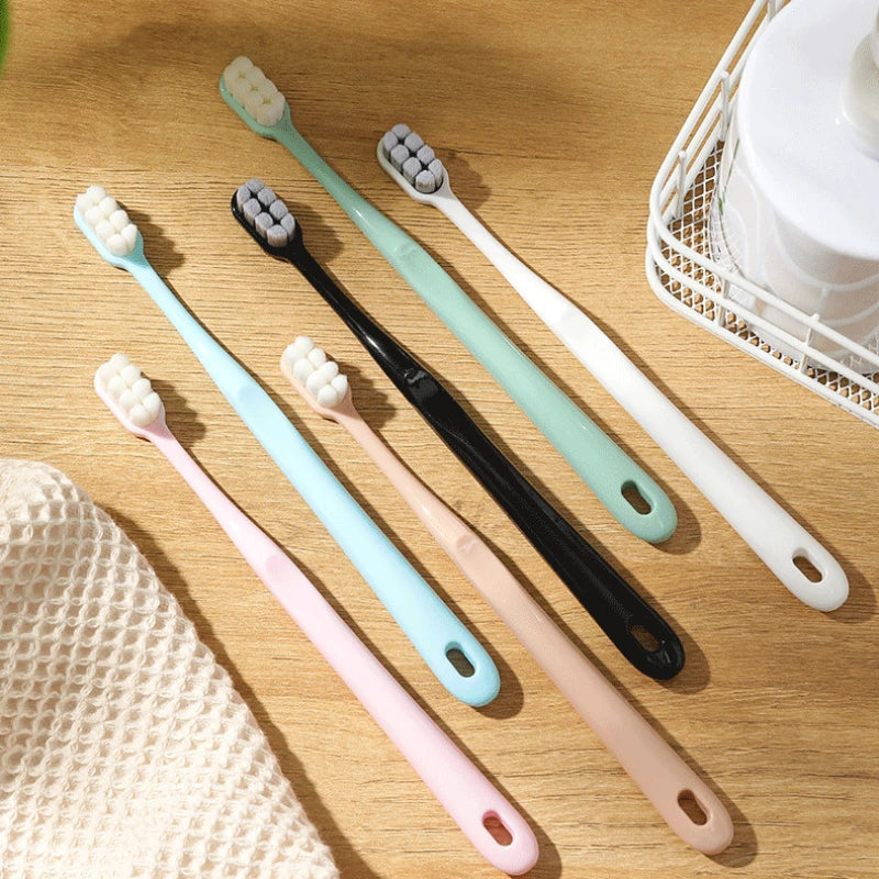 A collection of soft bristle toothbrushes in various pastel colors, including pink, mint green, and white, displayed on a woo