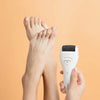 Un par de pies está siendo exfoliado con un archivo o exfoliador eléctrico blanco para pies.