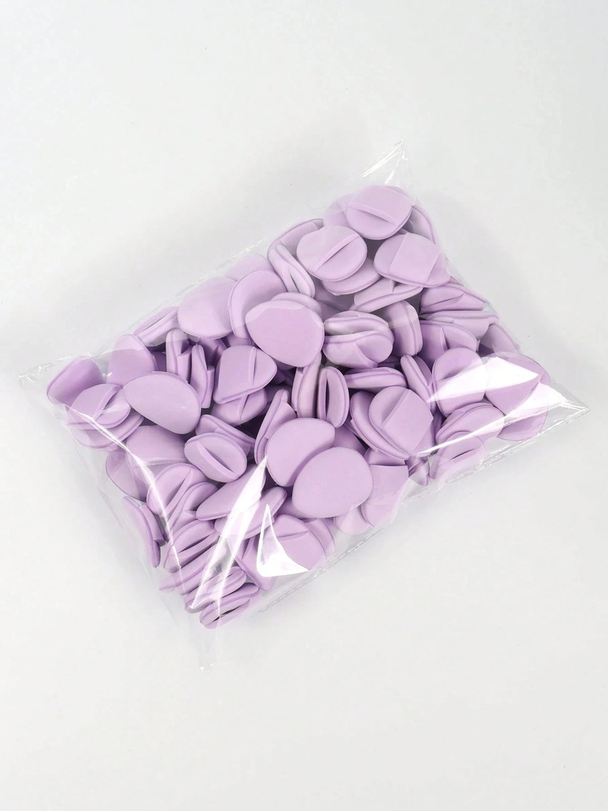 A clear plastic bag filled with purple latex-free finger puffs for makeup application.