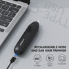 A black rechargeable nose and ear hair trimmer lying on a gray surface with charging accessories.