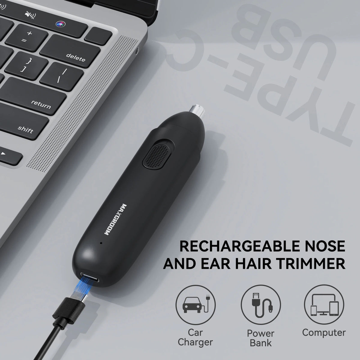 A black rechargeable nose and ear hair trimmer lying on a gray surface with charging accessories.