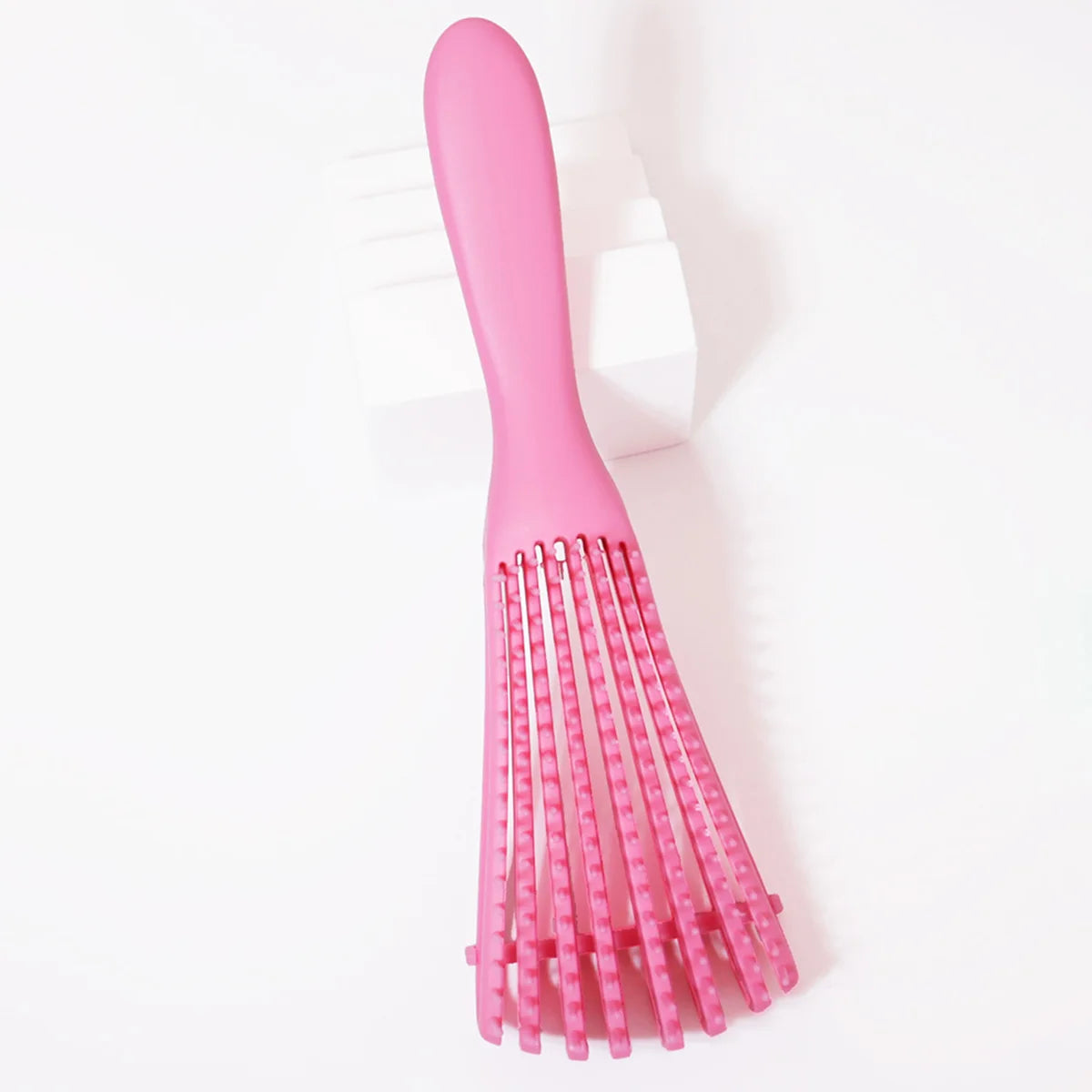 A pink adjustable detangling hair brush with multiple flexible bristles is shown against a white background.