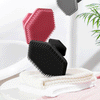A black silicone facial cleaning brush is resting on a white towel next to a pink cloth.
