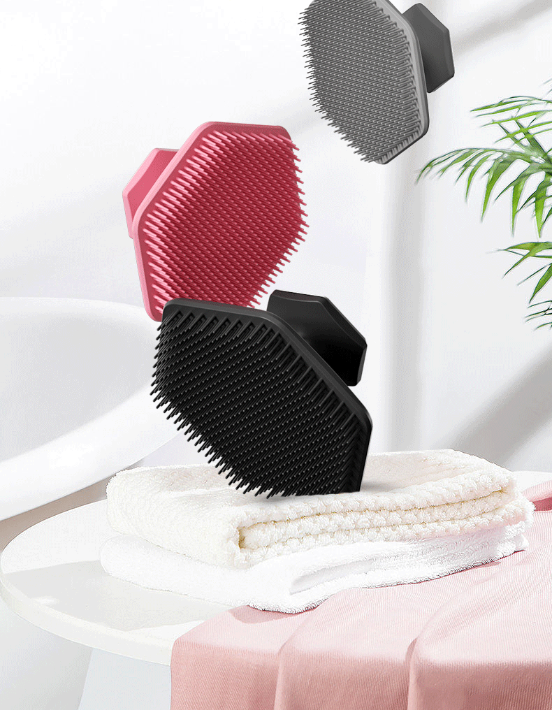 A black silicone facial cleaning brush is resting on a white towel next to a pink cloth.