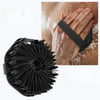 Un cepillo exfoliante de silicona natural y negra junto a una mano usando el producto.