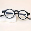 Une paire de lunettes de lecture claires à monture noire réglables posées sur une surface blanche.