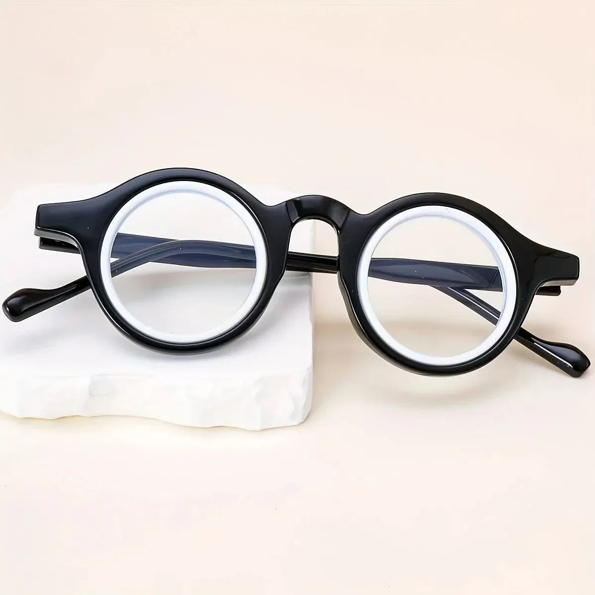 Une paire de lunettes de lecture claires à monture noire réglables posées sur une surface blanche.