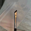 A close-up view of a professional angled makeup brush with a metallic finish resting on a translucent surface.
