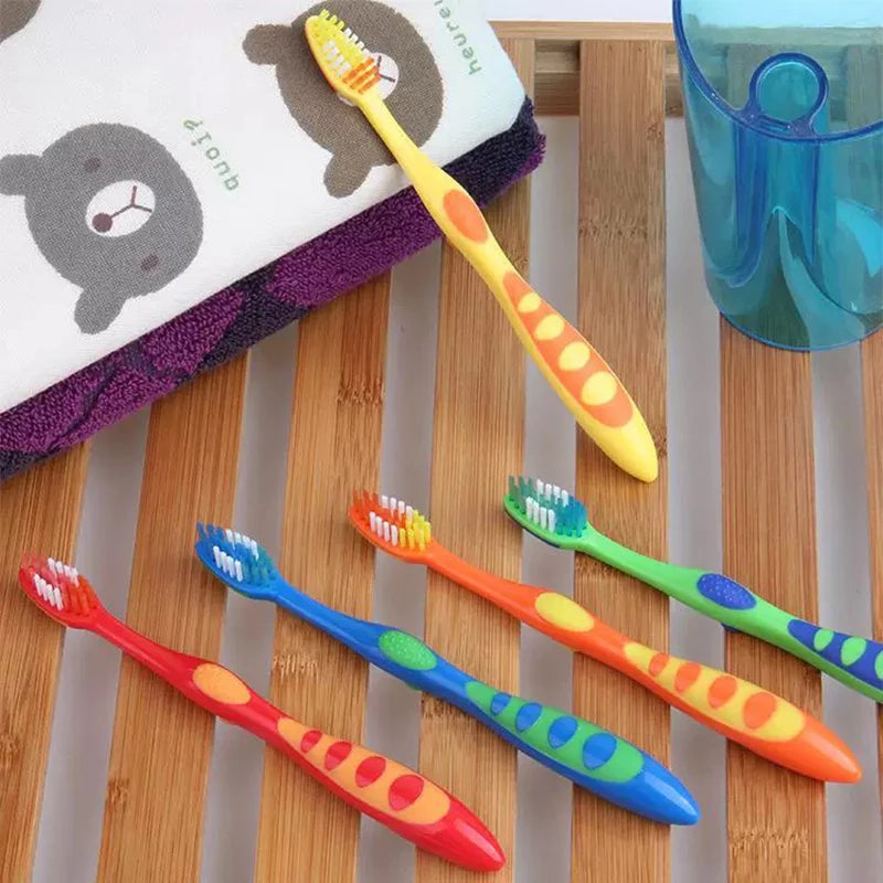 A set of five colorful children's dental toothbrushes with bright orange, yellow, and green handles resting on a wooden surfa