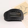A black oval flat hair clip with a slotted design is shown against a light background.
